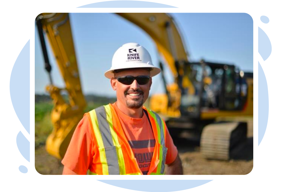 A smiling Knife River employee stands in front of an excavator